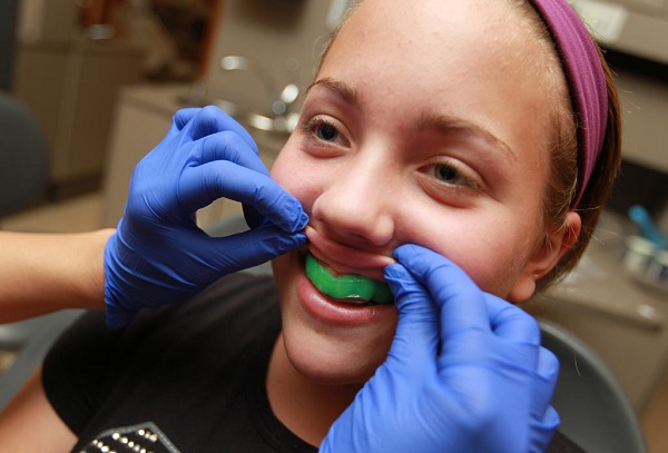 Dentist is putting on a mouth guard for a girl. The dentist's office is blurred in the background.