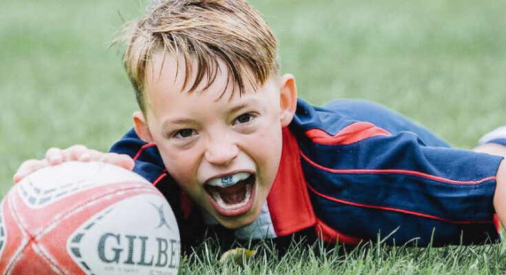 A boy is playing rugby. We can see a mouthguard in his open mouth.