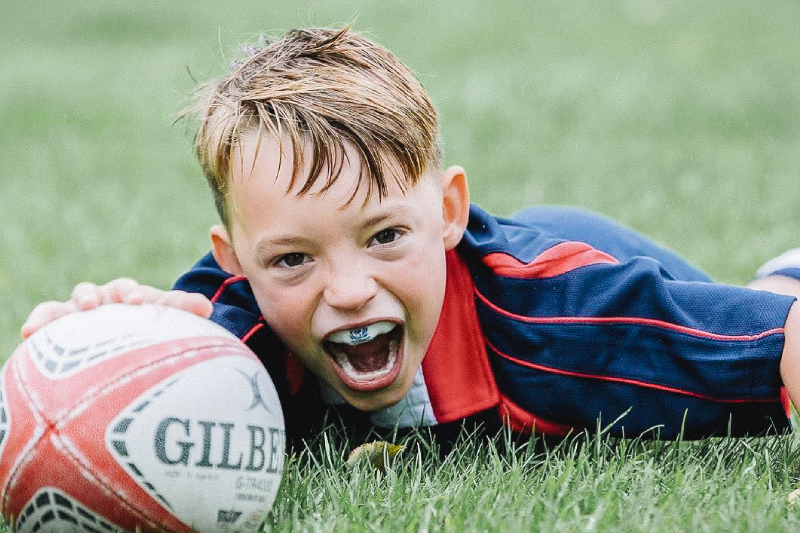 A boy is playing rugby. We can see a mouthguard in his open mouth.