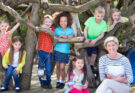 Small kids and their teacher are sitting under a tree