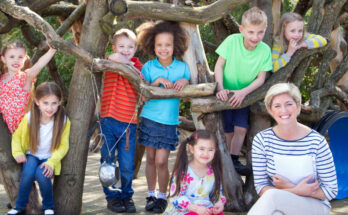 Small kids and their teacher are sitting under a tree